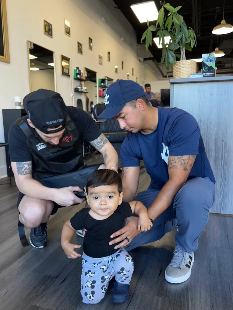 Two Victory Barbershop barbers teaming up to give a toddler his first haircut in Boca Raton