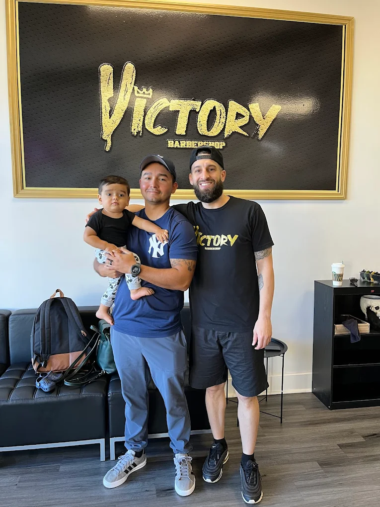 Gold Victory Barbershop crown sign on the wall with customers in the Boca Raton shop